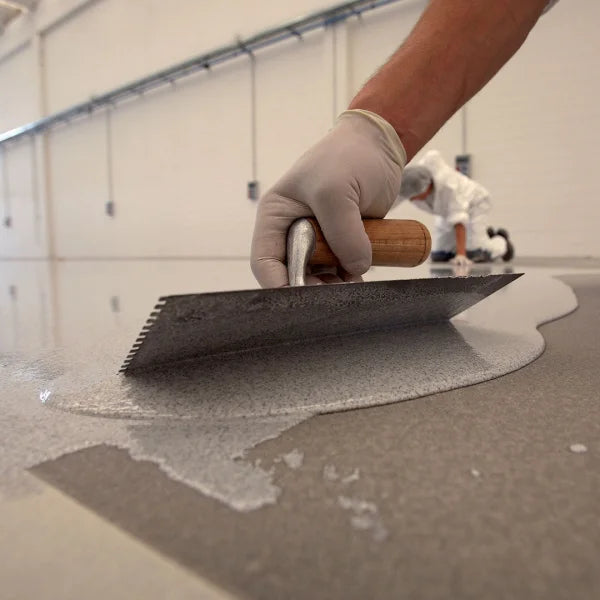 Close-up of MAPEFLOOR I 320 SL CONCEPT being applied with a notched trowel on a concrete floor in an industrial setting